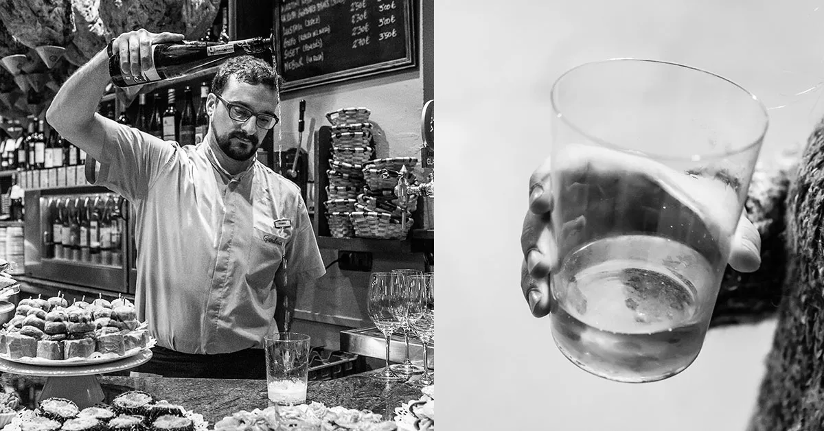 A bar tender in the Basque Country pours txakoli from high while surrounded by pintxos, or local tapas
